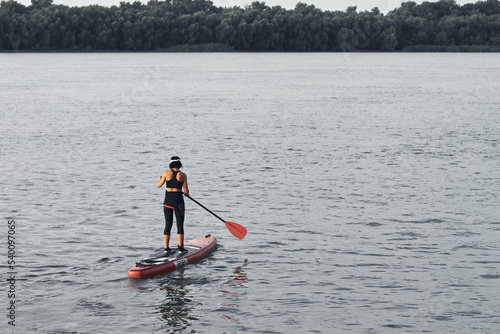 Back view of woman rowing on stand up paddle board (SUP) on river