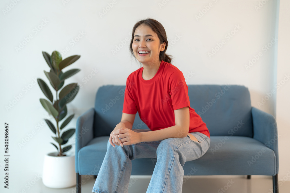 A beautiful woman in a red shirt sitting on the sofa happy smile. A beautiful woman in a red shirt sitting on the sofa happy smile.