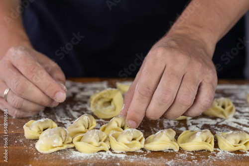 Chef cook hands making handmade Tortellini ravioli on wooden cut board with flour. Italian cuisine.