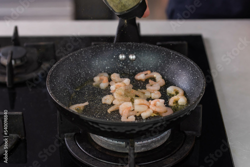 Chef cook hands roasting shrimps in wok pan with oil and spice. Seafood healthy cuisine.