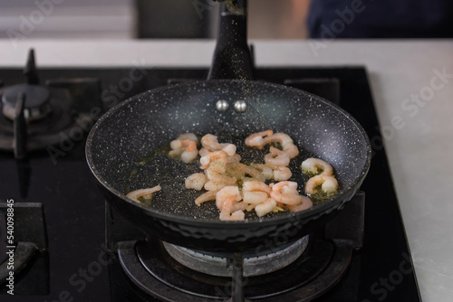 Chef cook hands roasting shrimps in wok pan with oil and spice. Seafood healthy cuisine.