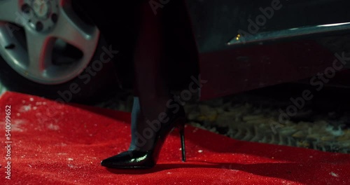 Close up of elegant woman in black high heels stepping on red carpet while going out of luxury car. Celebrity, wealth and modern lifestyles concept.