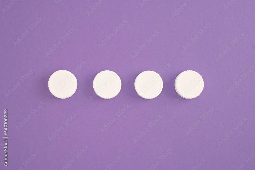 Top view of white plastic bottle caps lined up in a row on purple background Top view of white plastic bottle caps lined up in a row on purple background