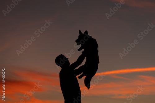 Silhouette of man holding his lovely corgi dog in arms at sunset. Pet and owner or master friendship. Love animals concept.