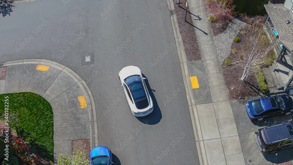 Aerial view of a white car leaving a home driveway and driving away; drone follow shot