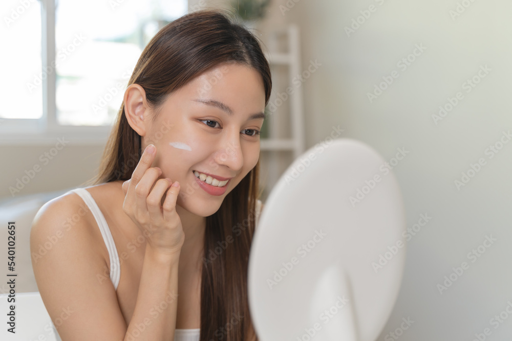 Asian young woman applying cream to her face in routine self care.