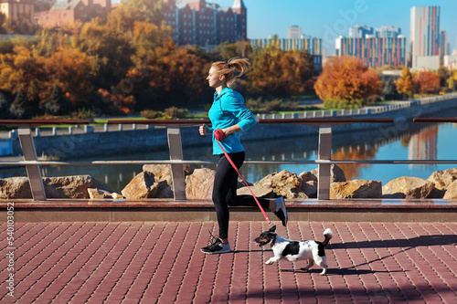 Side view picture of a woman jogging with her dog against city background