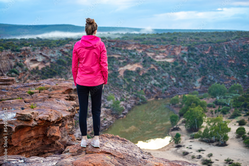 Fototapeta premium long-haired girl walks along a ridge on the red rocks of kalbarri national park in western australia; hiking in the wilderness, australian outback