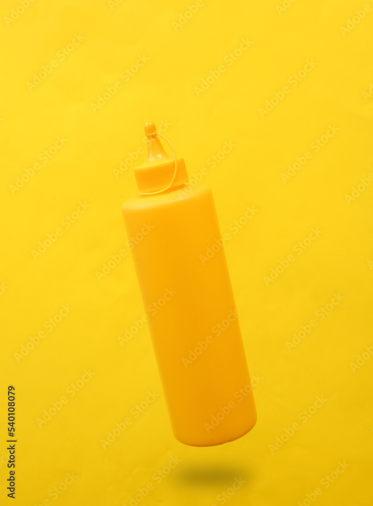 Yellow mustard bottle levitating on yellow background Yellow mustard bottle levitating on yellow background