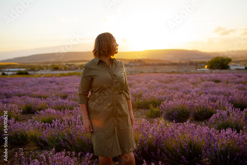 Fototapeta Naklejka Na Ścianę i Meble -  Beautiful plus size woman dressed dress and straw hat walking in the lavender flowers field, enjoy the aromatherapy