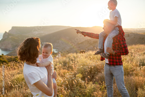 Happy family spending time together in the nature, mother father daughter and son have fun, playing with kids in vacation against the background the grass, mountain and sunset