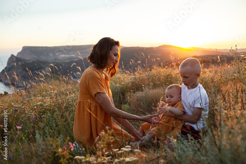 Happy family spending time together in the nature, mother and two kids, daughter and son have fun, woman playing with kids in vacation against the background the grass, mountain and sunset