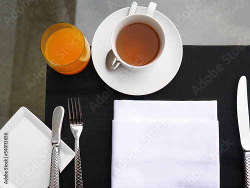 Top View of breakfast table, cup of hot tea, glass of orange juice, white napkin with tableware and eating utensils setting, fork, knifes, waiting for Meal photo