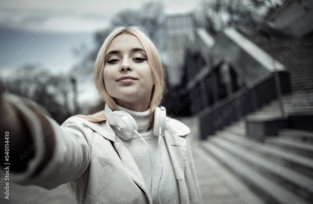 Young stylish girl with headphones makes selfie outdoors