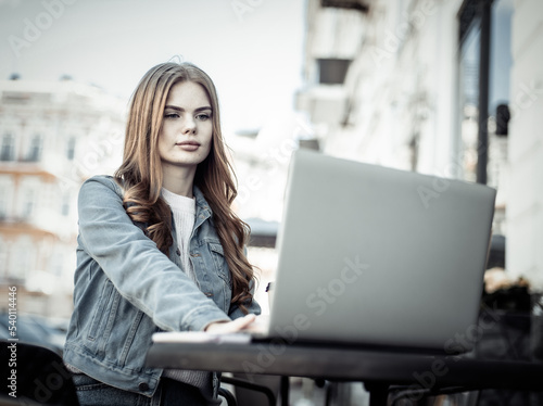 Young beautiful woman freelancer using laptop while sitting at table in outdoor cafe