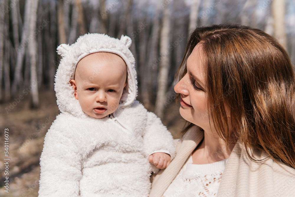A beautiful young mother in a white dress and a beige coat with a baby in a spring birch grove. High quality photo A beautiful young mother in a white dress and a beige coat with a baby in a spring birch grove. High quality photo