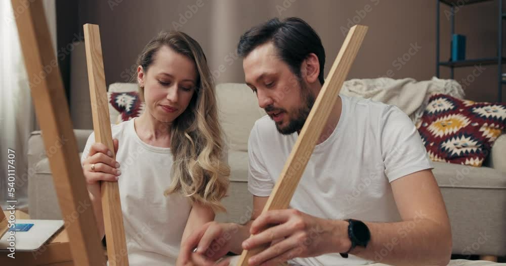 Serious concentrated woman and man trying to decorate furnish new wooden floor lamp moving in process happy family concept delighted husband and wife on carton boxes background. Serious concentrated woman and man trying to decorate furnish new wooden floor lamp moving in process happy family concept delighted husband and wife on carton boxes background.