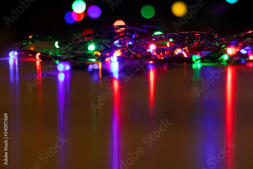 The multi-colored lights of the New Year and Christmas garland are reflected on the shiny surface of the table © Volodymyr