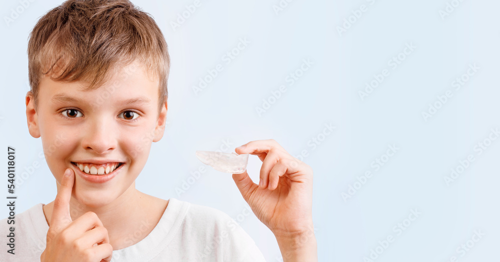 Positive child boy is holding mouth guards for his teeth and smiling. Banner. Invisible braces helps of orthodontics problem. Close-up portrait. Mobile appliance for dental teeth correction. Positive child boy is holding mouth guards for his teeth and smiling. Banner. Invisible braces helps of orthodontics problem. Close-up portrait. Mobile appliance for dental teeth correction.