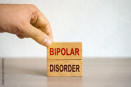 Hand puts blocks with the words Bipolar Disorder - manic depression. Mood disorder characterized by periods of depression and periods of elevated happiness. Mental disorder concept. Selective focus photo