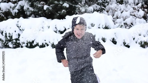 Cute young boy in winter clothes is playing with snow on back yard. Winter time