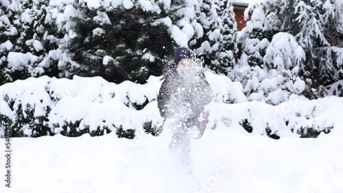 Cute young boy in winter clothes is playing with snow on back yard. Winter time