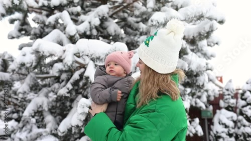 Pretty young woman in green winter coat is playing with her baby girl outside while snowing time. winter concept. Slow motion