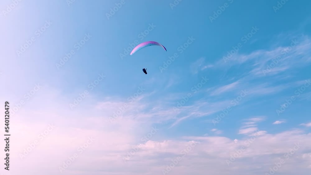The pilot of a paraglider on a cruise flies against the blue sky on a sunny day. aerial view The pilot of a paraglider on a cruise flies against the blue sky on a sunny day. aerial view