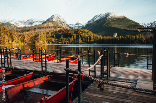 Red boats in port bounded in wooden mole on Strbske pleso lake in High Tatras - Slovakia in autumn time. Beautiful and colorful sunrise on lake with boats and white snowy moutanins on background photo