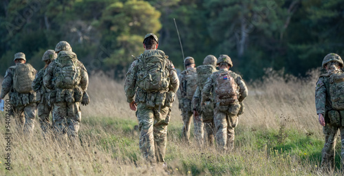 8 male and female British army soldiers tabbing with 25Kg bergens across open countryside, Wiltshire UK photo