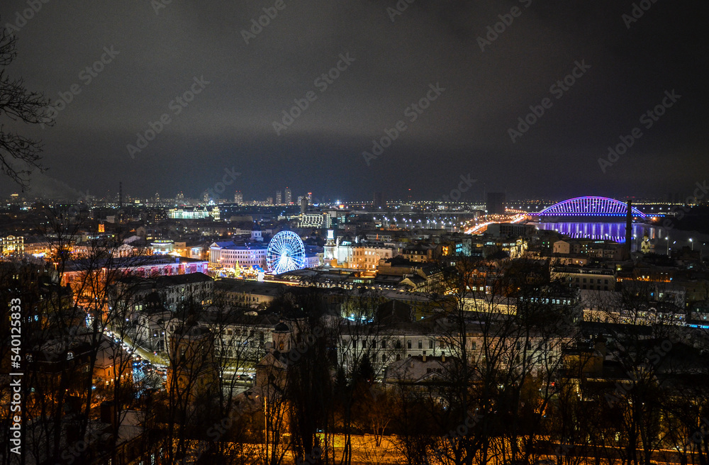 Fototapeta premium Aerial evening view to Kontraktova Square with Christmas market, New Year tree and ferris wheel during celebration. Kyiv, Ukraine