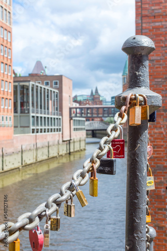 On an old link chain of the Speicherstadt in Hamburg hang many colorful so-called love locks in different shapes. The chain stands out against background.