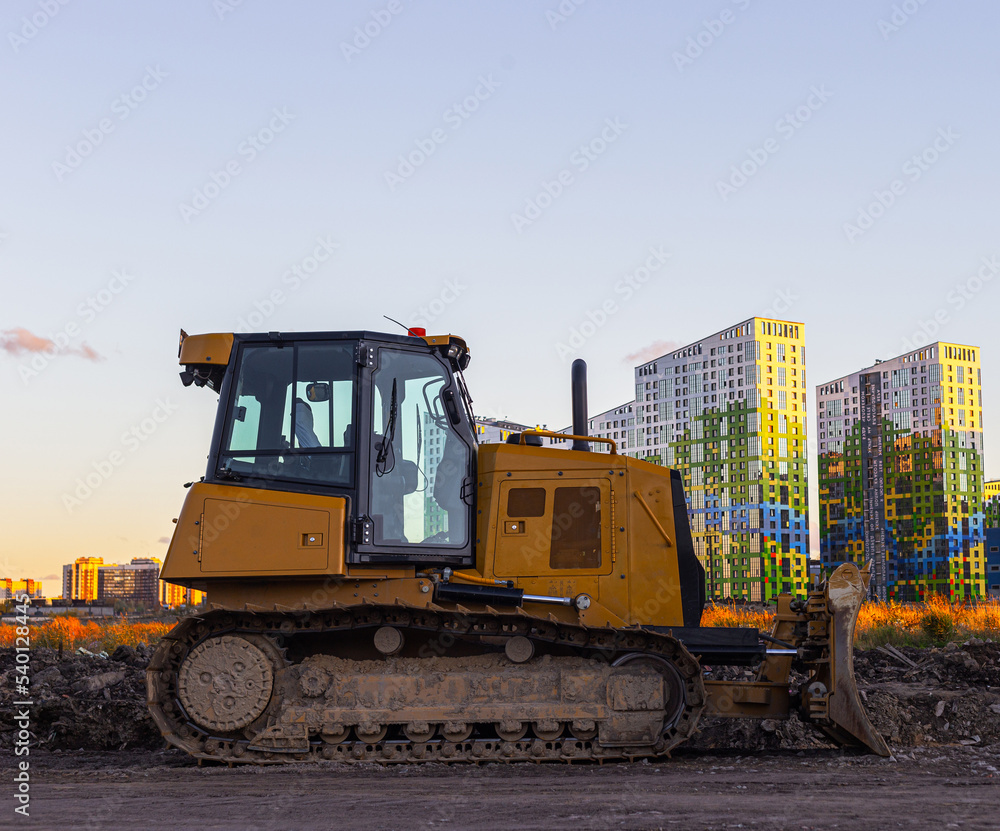 Parked, yellow crawler bulldozer side view against the backdrop of the urban landscape. Parked, yellow crawler bulldozer side view against the backdrop of the urban landscape.