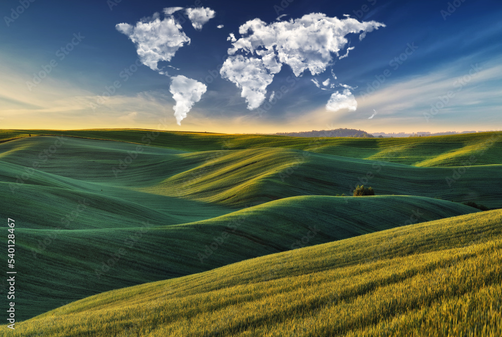 Obraz premium clouds in the form of a world map over a green field. Travel and landscape concept. hilly field