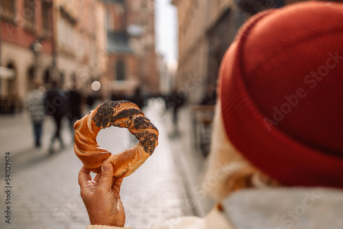 Tourist woman hand holding bagel obwarzanek, traditional polish snack on Market square in Krakow, Europe. Back view photo