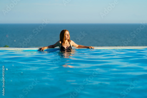 A beautiful woman in a black swimsuit by the side of a panoramic pool. 