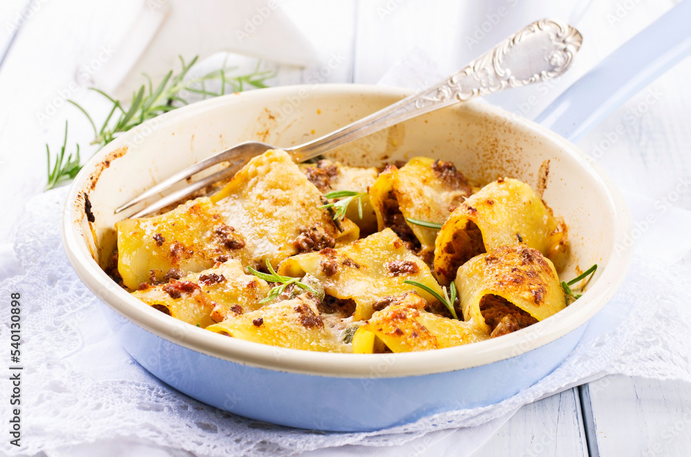 Traditional Italian paccheri pasta filled with minced meat and served with parmesan as close-up in a design pan Traditional Italian paccheri pasta filled with minced meat and served with parmesan as close-up in a design pan