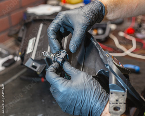 The master in black gloves changes the bulb in the headlight of the car. Car headlight during repair and cleaning.The mechanic restores the headlight of the car. Restoration of automotive optics.