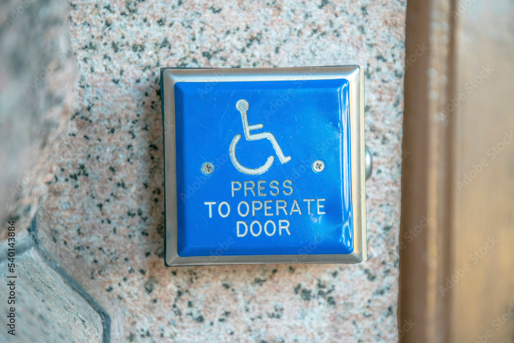 Blue handicapped access entrance pad for door mounted to a wall in Austin Texas
