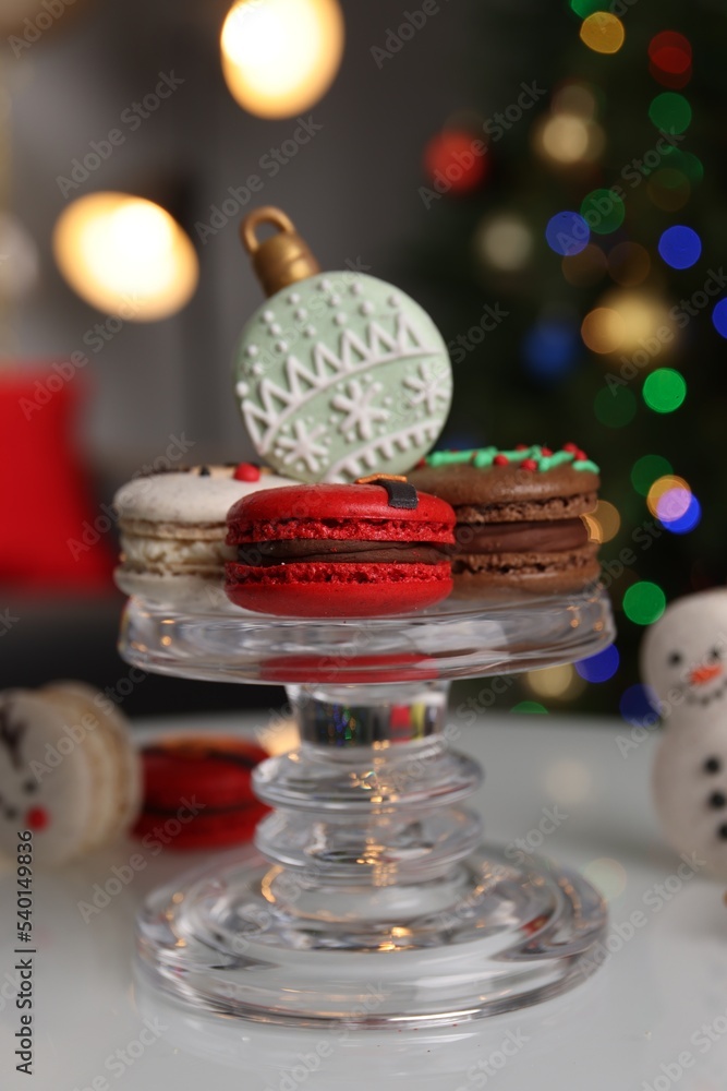 Beautifully decorated Christmas macarons on white table against blurred festive lights