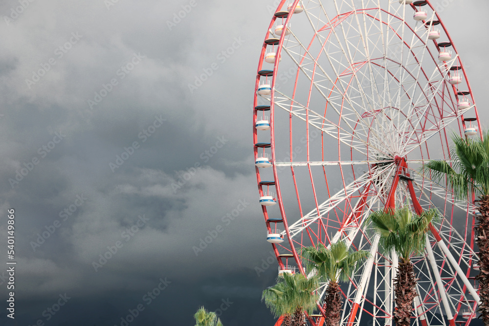 Beautiful large Ferris wheel and palms against heavy rainy sky outdoors. Space for text