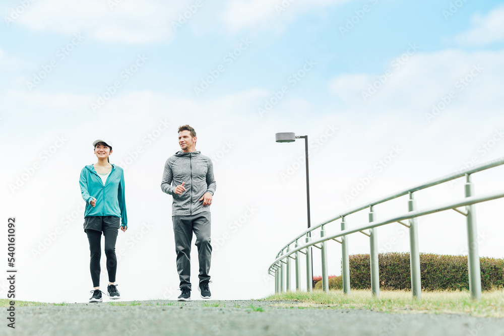 健康のため朝公園でウォーキング・散歩・有酸素運動するスポーツウェアを着たアジア人の男女
