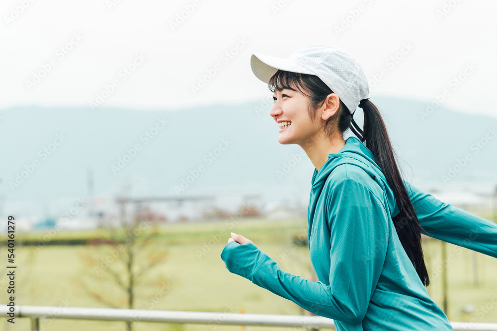 健康管理のため公園を笑顔で有酸素運動するスポーツウェアの元気なアジア人女性
