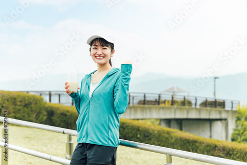 ボディメイクのため公園でプロテインを飲みながらトレーニングするスポーツウェアのアジア人女性  © buritora