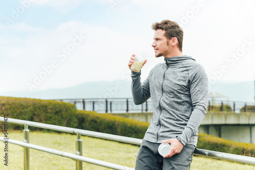 公園で運動中にプロテインを飲んで栄養補給するスポーツウェアの白人男性（笑顔）

 photo