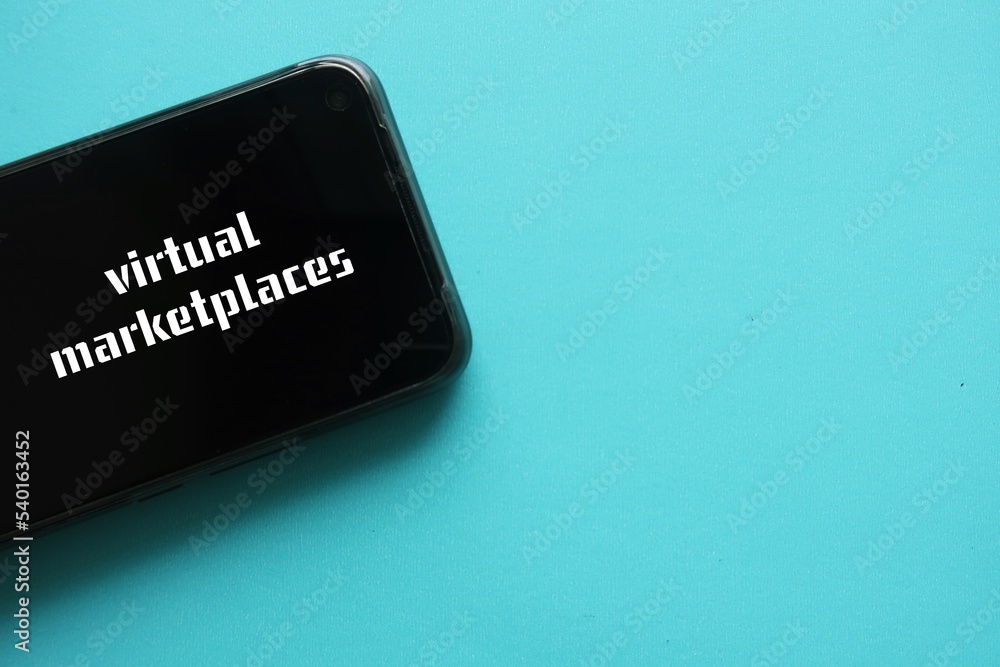 Mobile smartphone on copy space blue background with text on screen VIRTUAL MARKETPLACE - means e-commerce site that connects sellers with buyers or virtual store to buy or sell products and service Mobile smartphone on copy space blue background with text on screen VIRTUAL MARKETPLACE - means e-commerce site that connects sellers with buyers or virtual store to buy or sell products and service