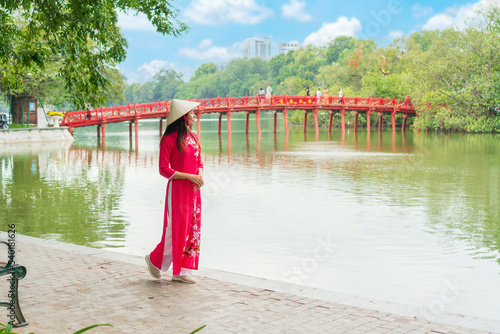 Young Asian woman tourist wearing Ao Dai (traditional Vietnamese dress) sightseeing at the Red Bridge in Hoan Kiem Lake, Hanoi, Vietnam. Copy space photo
