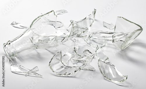 A glass bottle broken into many fragments on a light gray background.