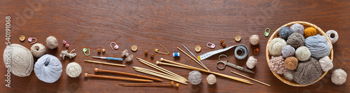 Hand knitting accessories: knitting needles, crochet hooks, skeins of woolen yarn, tips, scissors, pins and buttons on wooden table. Banner, panorama. Craft and DIY concept. Flat lay, copy space