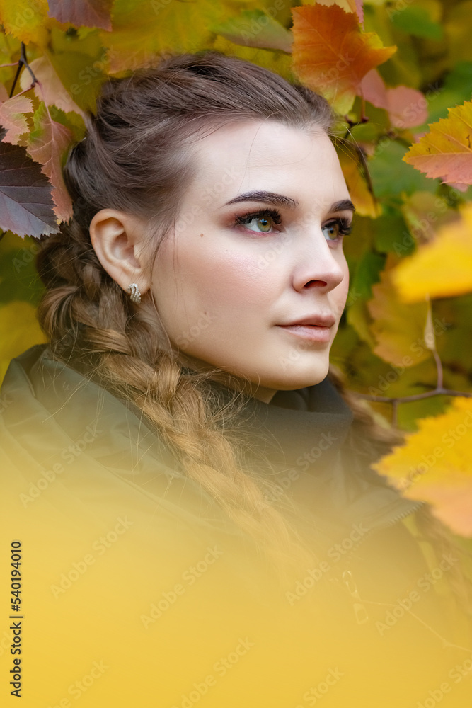 A beautiful serious girl stands near a tree with yellow foliage. A beautiful serious girl stands near a tree with yellow foliage.